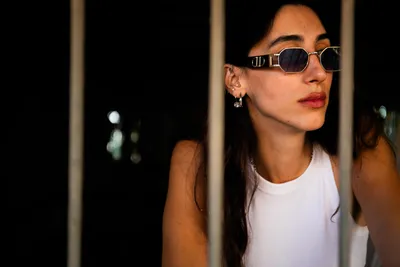 בחורה_עם_מששקפי_שמש_עומדת_מאחורי_חלון_עם_סורגים_צילומי_תדמית