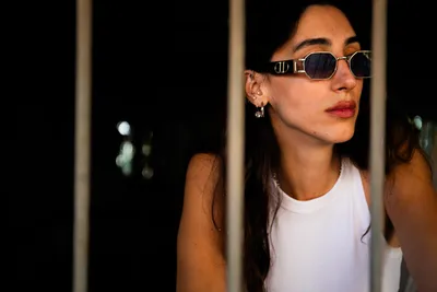 בחורה_עם_מששקפי_שמש_עומדת_מאחורי_חלון_עם_סורגים_צילומי_תדמית