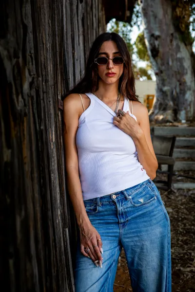בחורה_בחולצה_לבנה_וג׳ינס_עומדת_ליד_קיר_עץ_בוק_אישי